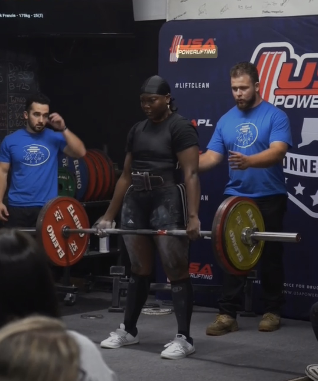 Khadijat lifting a loaded barbell on a platform at a USA Powerlifting meet