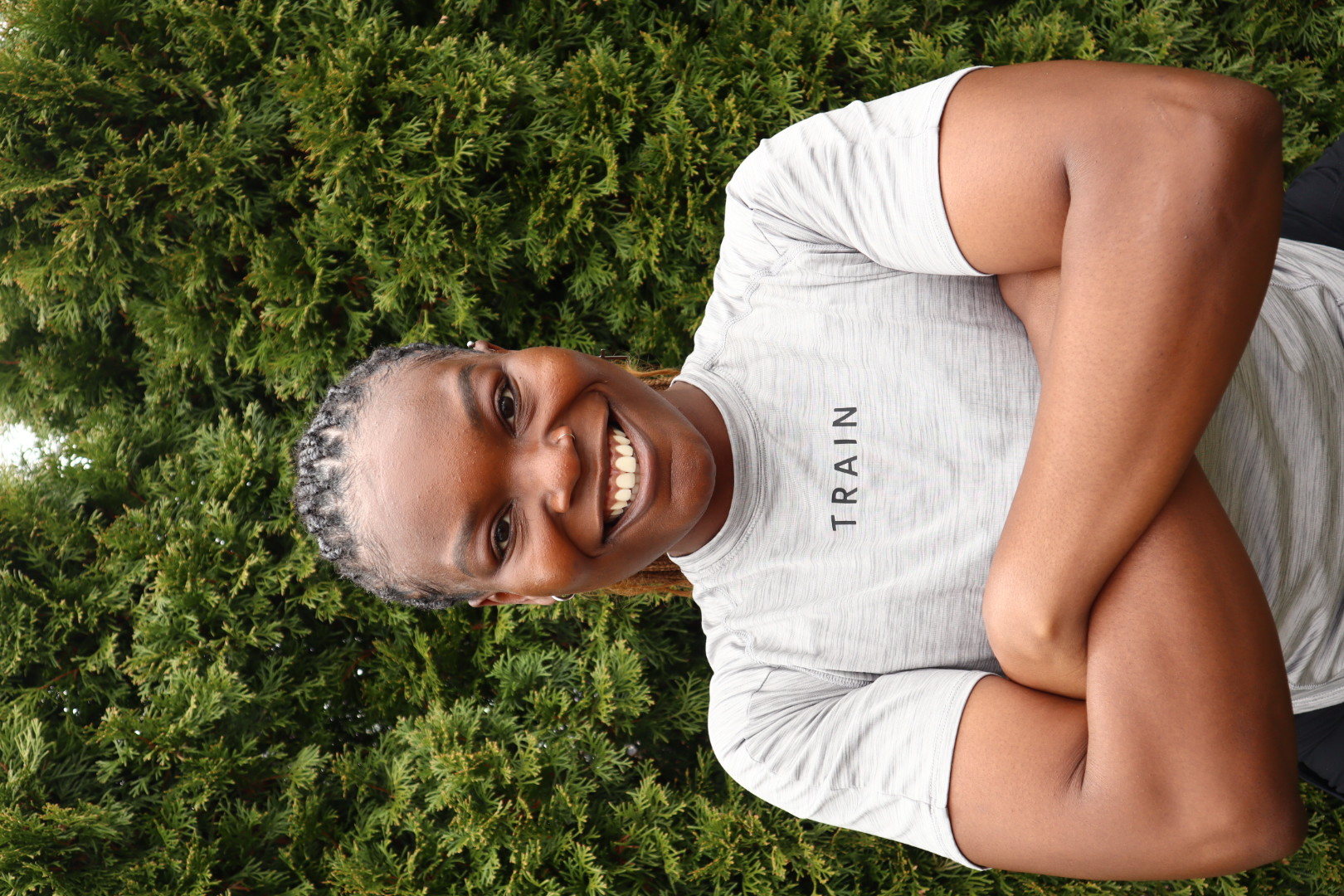 Khadijat standing outdoors with her arms crossed in a shirt that reads TRAIN