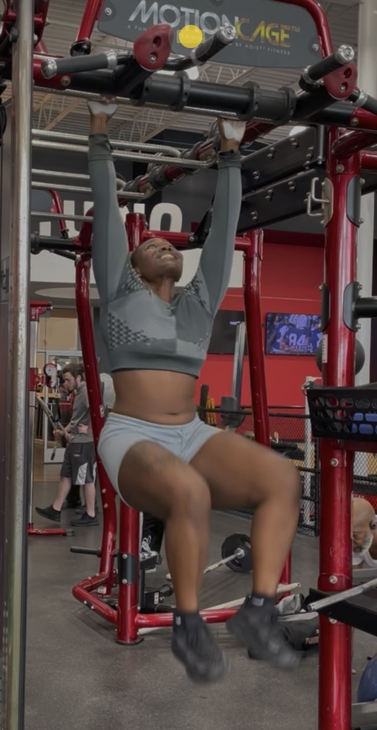 Khadijat hanging from a pull-up rig doing knee raises